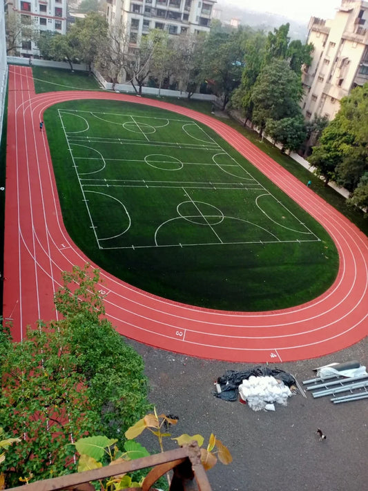 Bharat Natural running track installation — aerial view of red EPDM synthetic track with artificial turf infield at an urban school in India